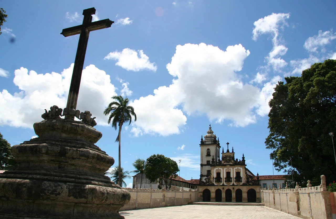 cruz com igraja ao fundo e céu azul em João Pessoa
