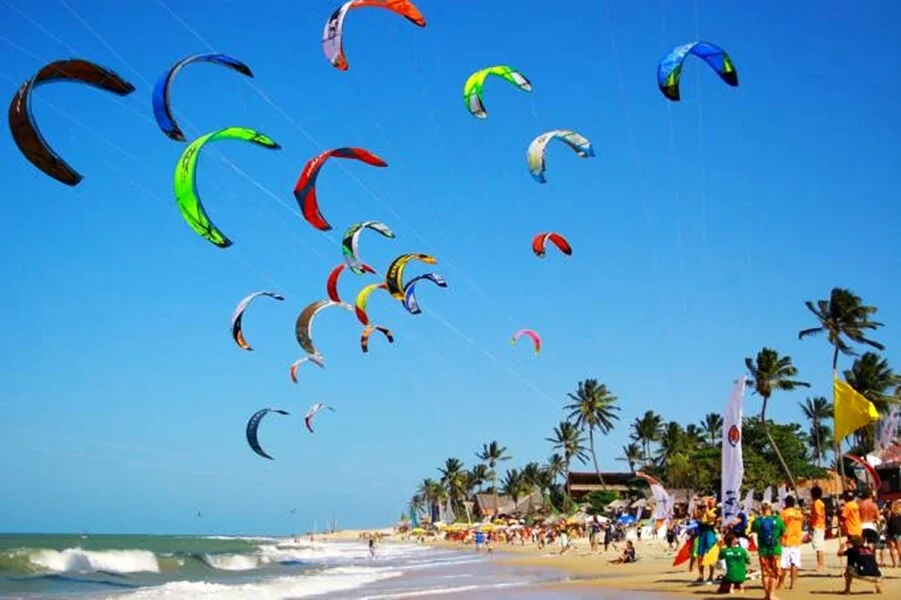 praia em Fortaleza com pessoas na areia e muitas pipas de kite e wind surf no céu