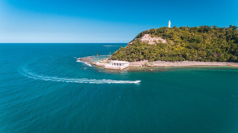 lancha no mar passando em frente ao forte e farol ao fundo em Morro de São Paulo